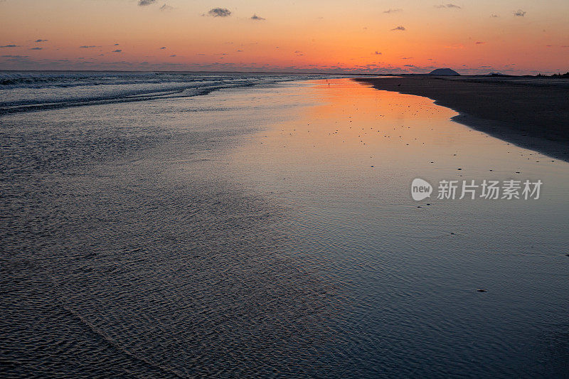 在日落后的海滩上，橙色的辉光在沙滩上反射出浅浅的海浪