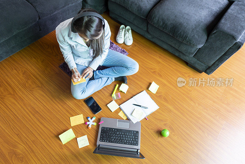 一个年轻女子坐在她客厅的地板上，一边听老师的指示一边做她的家庭作业