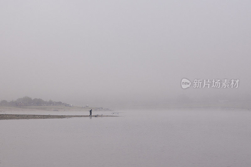 极简抽象的单色水景。鸟瞰图在一个大的山上湖泊与雾和一个渔民剪影在海岸线。