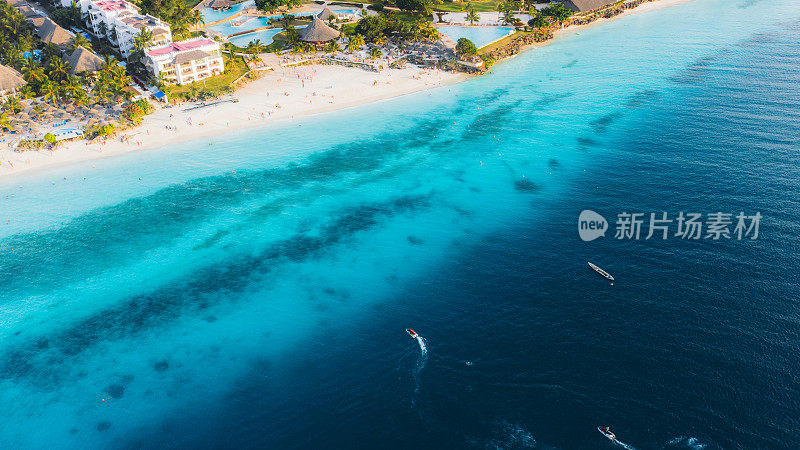 鸟瞰图美丽的海滩与蓝绿色的海洋，一群船，鳟鱼游泳在海洋和酒店在桑给巴尔岛，坦桑尼亚