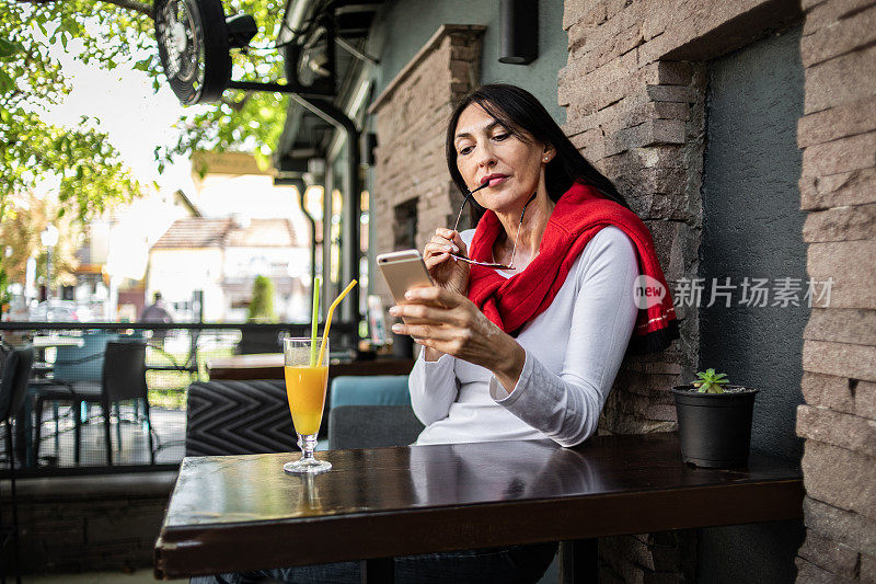 一个漂亮的女人在咖啡馆喝果汁。一个成熟的女人在自助餐厅喝着鲜榨橙汁，看着她的手机。