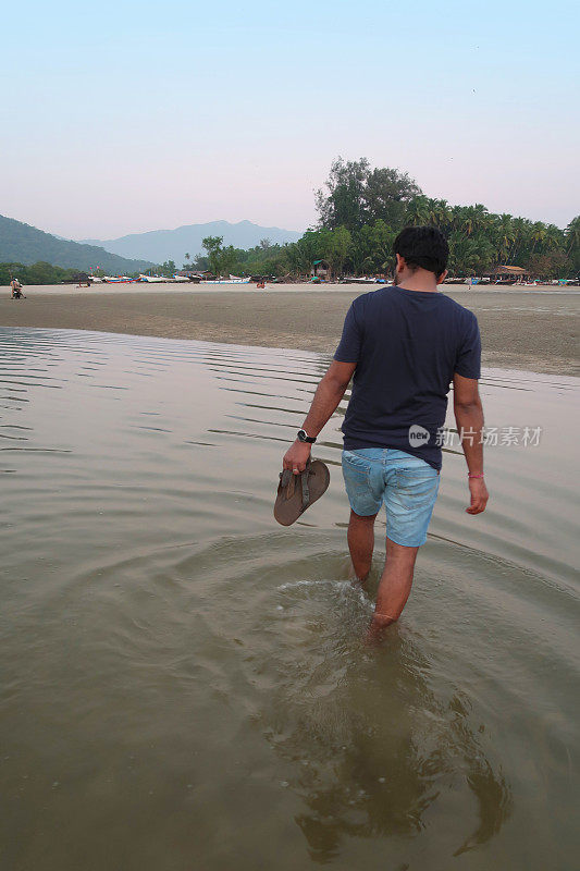 印度男子在海滩度假，从后面看到走出大海，从印度洋回到海滩，海浪翻滚到沙子，帕洛伦海滩，果阿，印度