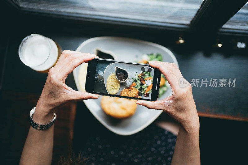 一名女子在餐馆用智能手机拍摄牛肉派