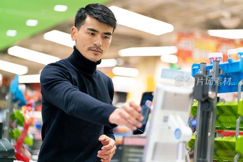 亚洲男性顾客用手机扫描非接触式自助支付的密码