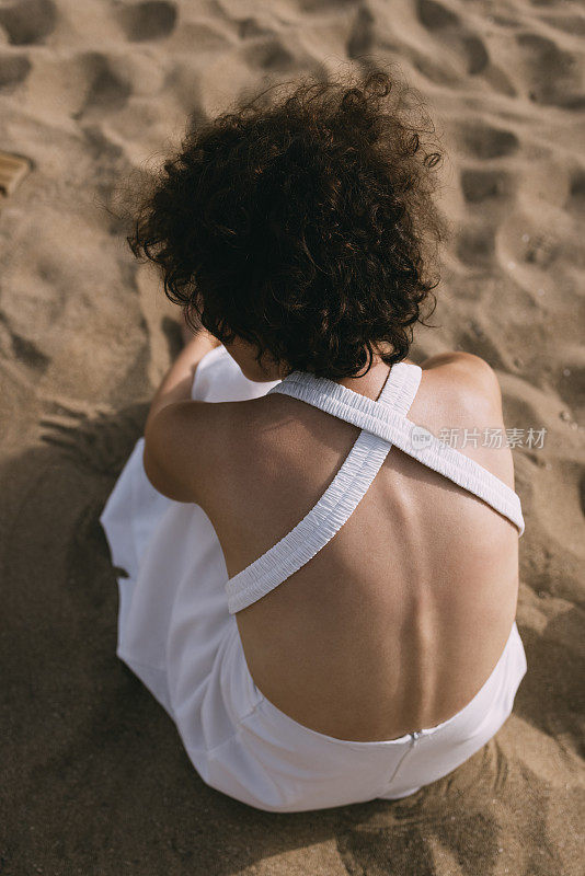 一个陌生的年轻女子穿着白色的裙子，坐在沙滩上的沙子上