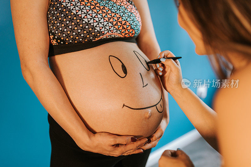 怀孕的女人正在画她怀孕闺蜜的肚子