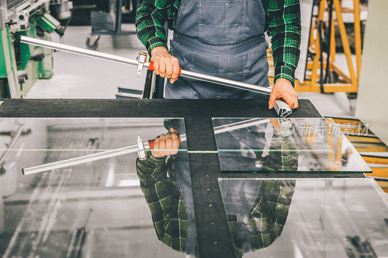 玻璃工人站在切割玻璃面板与专业切割设备，切割玻璃面板在工厂