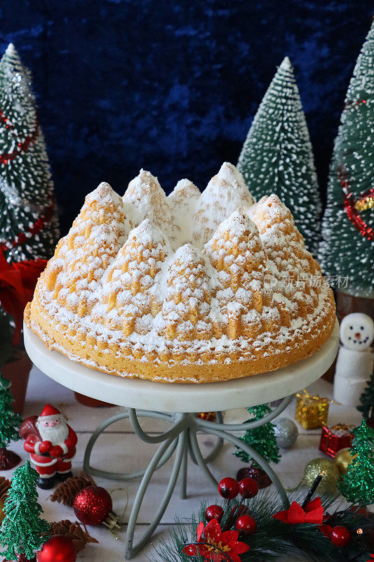 特写图像自制，圣诞树形状，柠檬细雨Bundt蛋糕在白色，大理石和金属蛋糕站周围的圣诞装饰，圣诞老人，柠檬口味的环海绵覆盖糖霜，蓝色背景