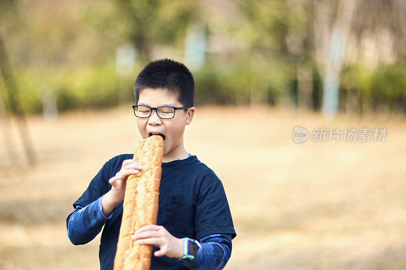 快乐的东亚男孩正在户外吃面包