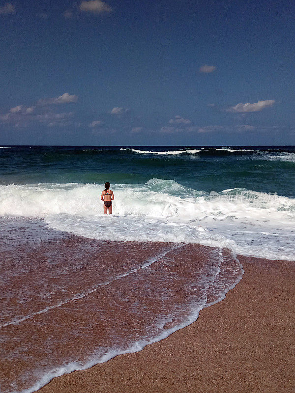 年轻的女孩在阳光明媚的夏日里跳着波浪