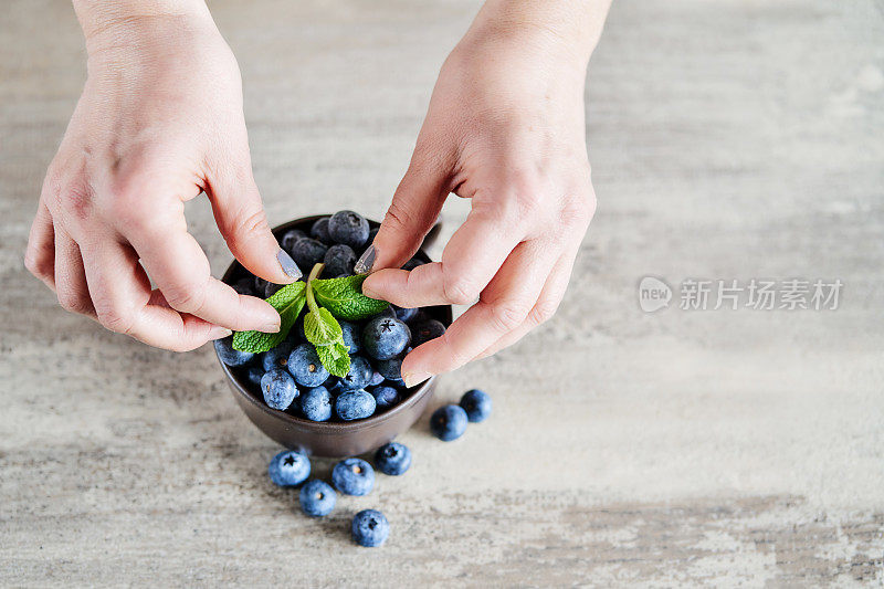女性的手把新鲜的薄荷放在碗上面的蓝莓