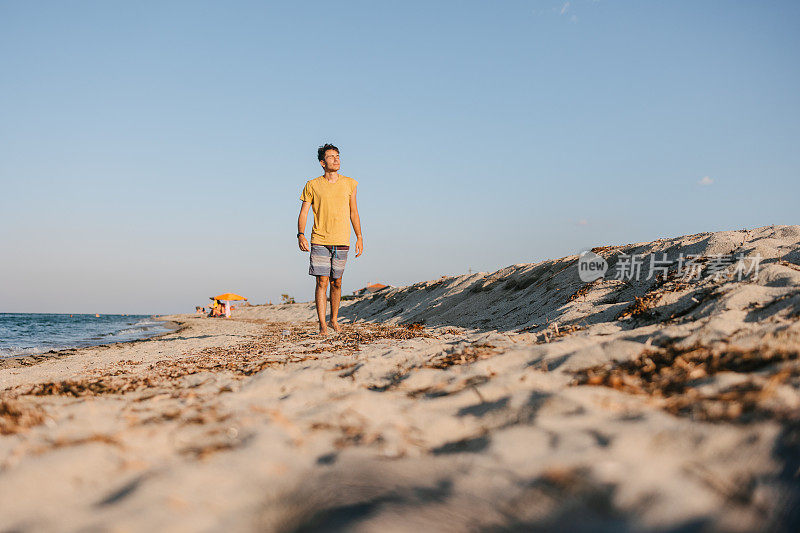 一个英俊的年轻人在日落时沿着海岸散步