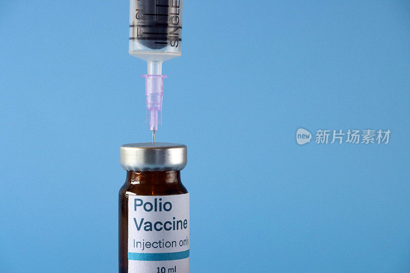 脊髓灰质炎(脊髓灰质炎病毒)疫苗的特写图像，标签为玻璃瓶，用于填充注射器，蓝色背景，聚焦前景