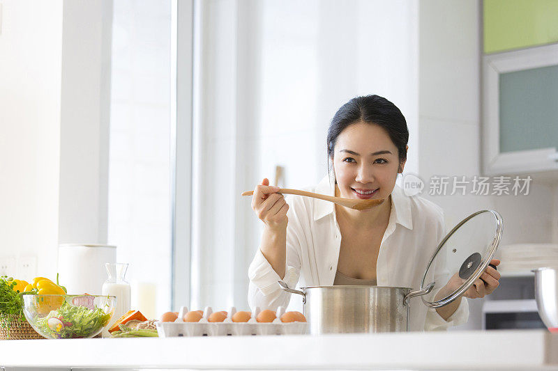 年轻的家庭主妇在厨房里品尝食物的照片