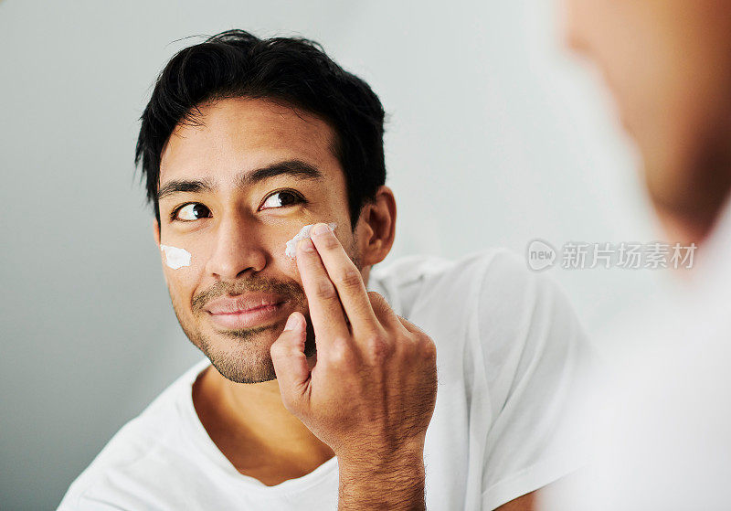 年轻男性在早上的护肤过程中使用面霜。一个有吸引力的健康男子使用皮肤美容产品的肖像。一个快乐的男人在做面部护理。