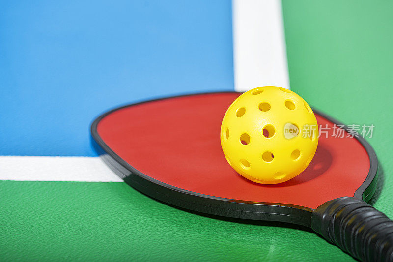 一个红色的匹克球球拍和一个黄色的球放在球场上