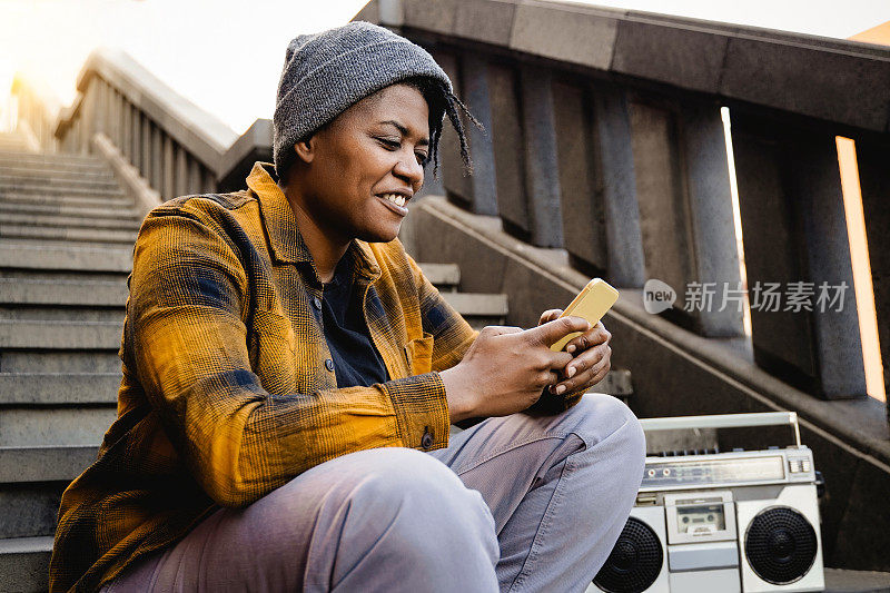 快乐的非洲女孩与嘻哈风格使用手机旁边的老式录音机户外-青年文化生活方式-注重面子