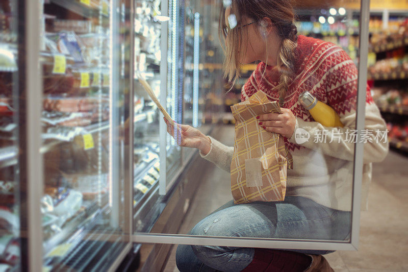 女性打开超市冷冻室挑选要买的东西。在杂货店买食物