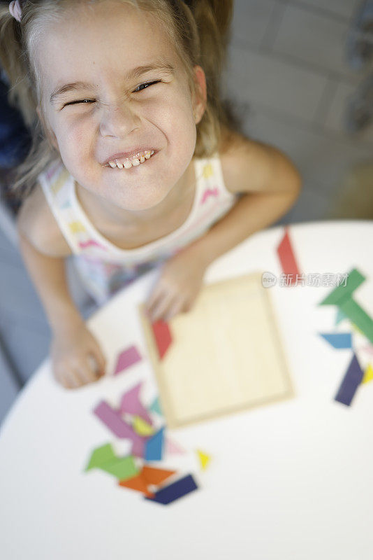 金发小女孩在家里玩七巧板的笑脸。肖像与选择性聚焦在她的脸和散焦背景。