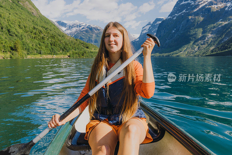 在挪威风景优美的Lovatnet湖上，微笑的女子在橙色独木舟的正面视图