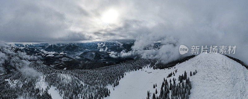壮丽的雪山全景照片，云雾缭绕的山顶和冬天脚下的森林