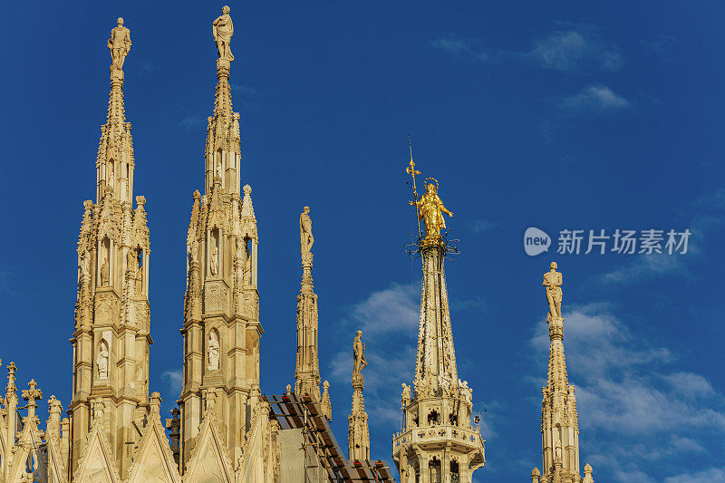意大利米兰，哥特风格的罗马天主教大教堂的屋顶在同音主广场，与圣母玛利亚雕像，小圣母，圣母玛利亚金色艺术品可见蓝天。