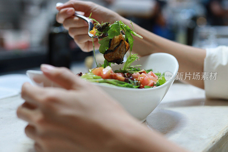 这张照片拍摄了一位亚洲女性在餐厅享用健康的混合沙拉，代表了清洁饮食、节食和健康食品的概念。