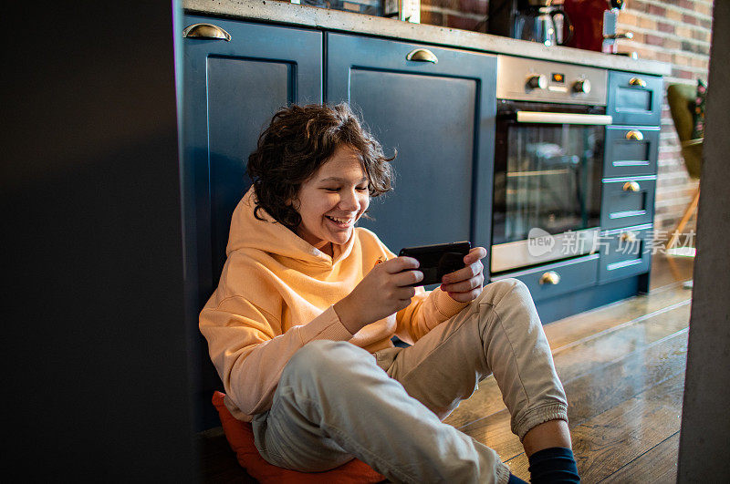 小男孩坐在厨房地板上玩智能手机