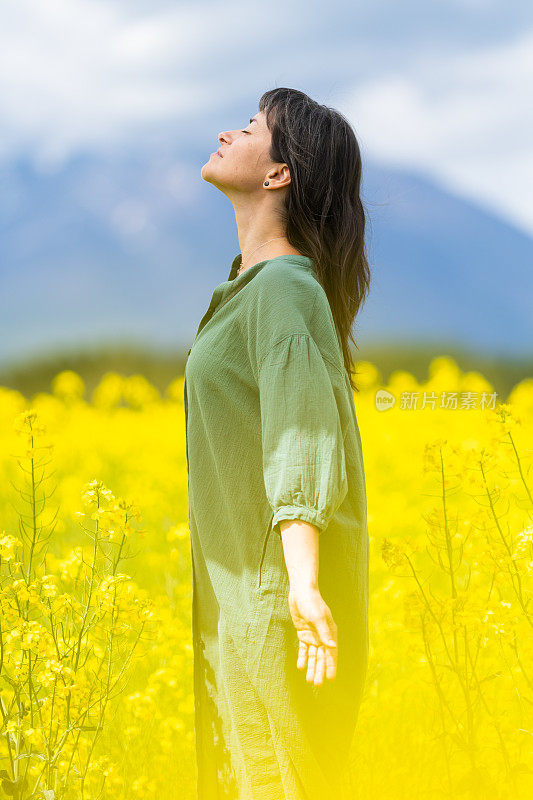 一位妇女在一片黄色的油菜花地里沉思，享受户外的乐趣