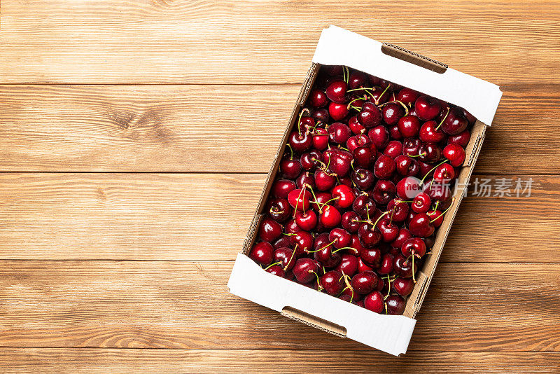 木桌上的纸板箱里装满了红樱桃。销售樱桃。健康的浆果