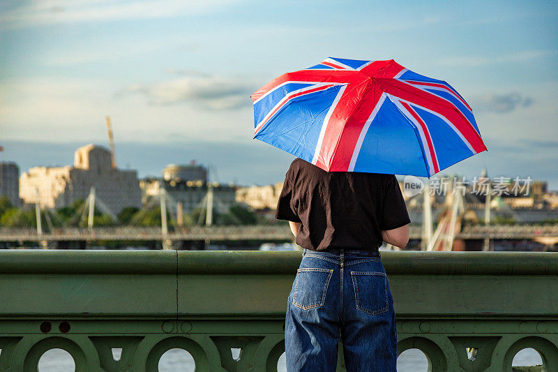 在伦敦市中心的威斯敏斯特桥上，一名女子手持英国国旗伞眺望风景