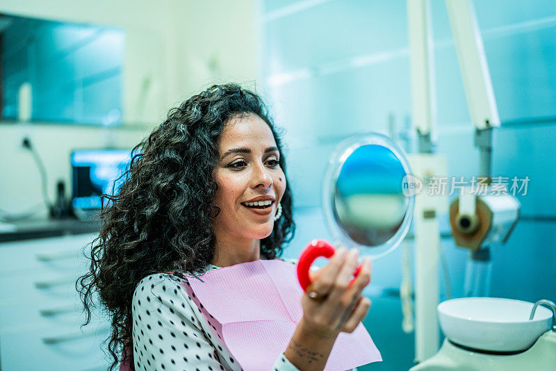 一位中年妇女在牙医诊所对着镜子看自己的牙齿