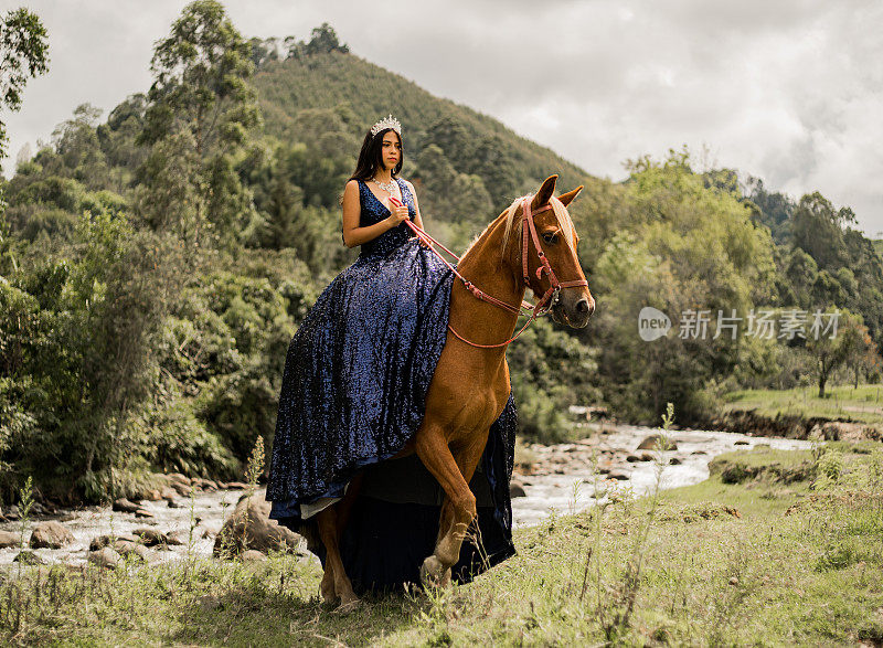 年轻女子穿着quinceañera连衣裙，头上戴着头饰，骑着她的马，在大自然中间的河边。