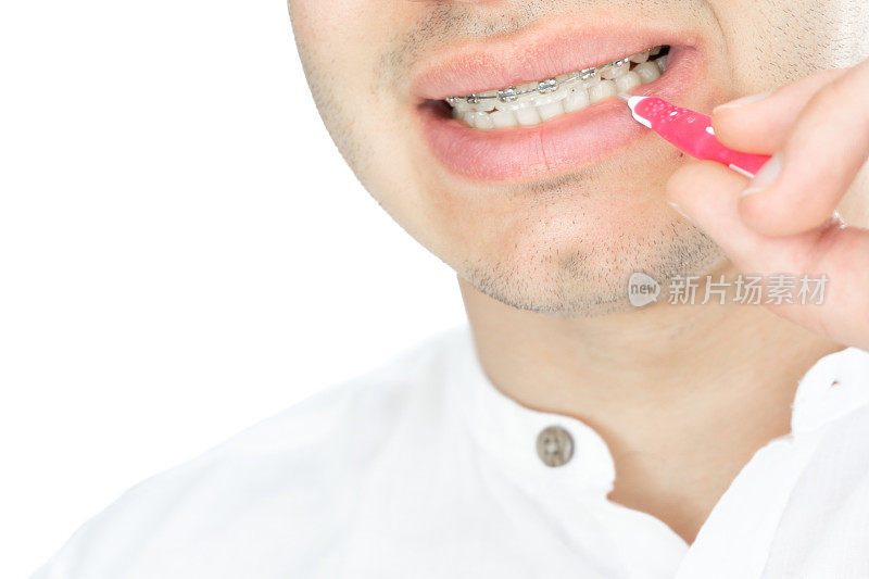 近距离的英俊的年轻人微笑着用漂亮的直白牙齿和牙套清洁牙齿，用牙间刷隔离在白色的背景上，直白的牙齿和牙套