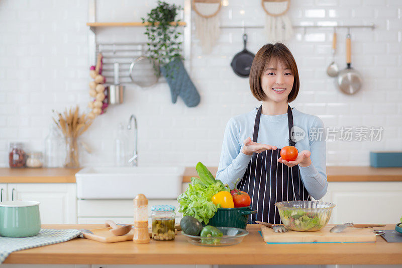 穿着围裙的亚洲年轻女性周末在家厨房准备烹饪沙拉蔬菜，女性制作沙拉，食物与营养，女性与健康的饮食，生活方式理念。