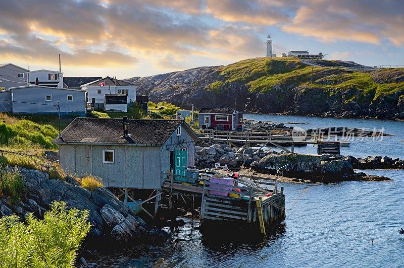 海岸上的房屋和渔具仓库以及远处的灯塔，位于加拿大纽芬兰的巴斯克海峡港