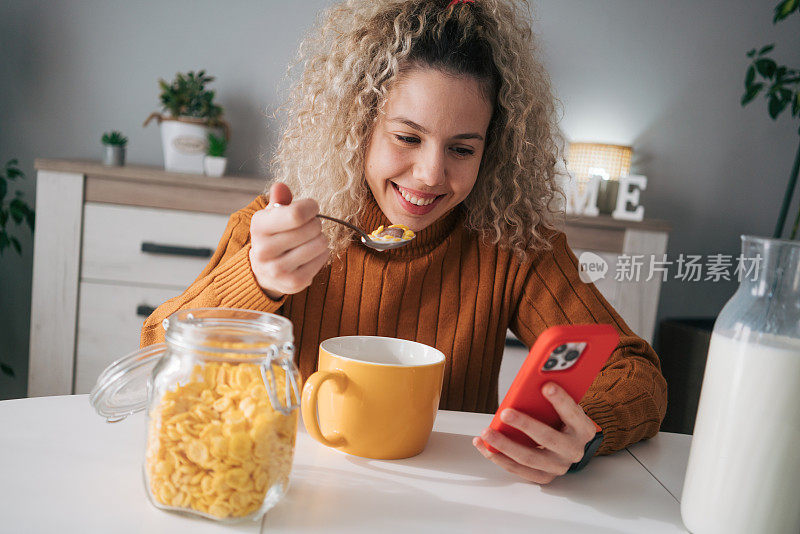 卷发的女人一边吃早餐一边用手机