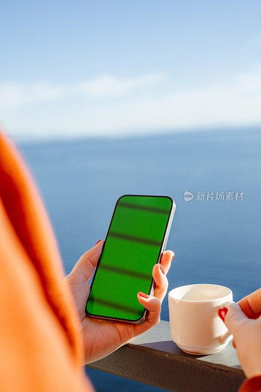 小女孩在海边阳台上用绿屏手机拍照