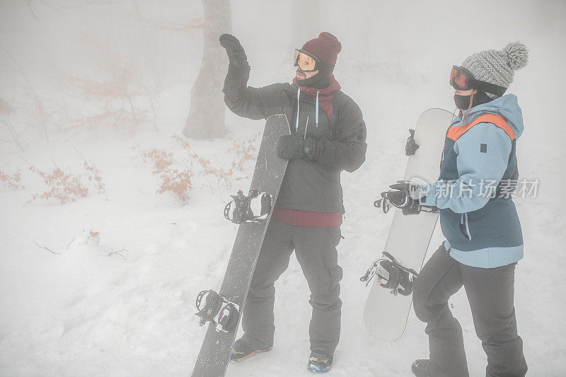 在一个雾蒙蒙的冬日，两个滑雪板运动员计划在山上玩滑雪板