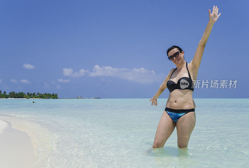 美丽的女人站在浅水与一只手，在小岛屿的海滩在四月，马尔代夫