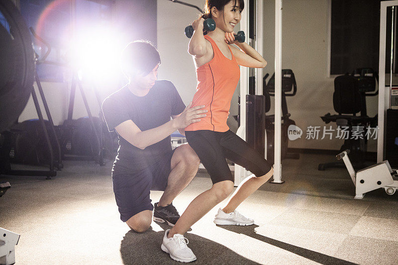 一个年轻的女人正在用哑铃做肌肉训练。一个女人在健身俱乐部做伸展运动。男性教练在教学。