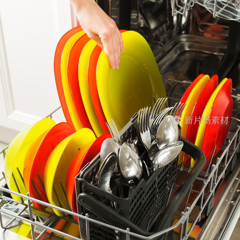 女用手把干净的彩色盘子放在开着的洗碗机里