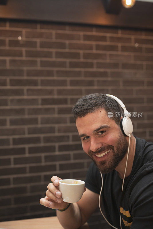 留着胡子的时髦帅哥，戴着耳机，在咖啡馆餐厅的咖啡休息时间喝咖啡