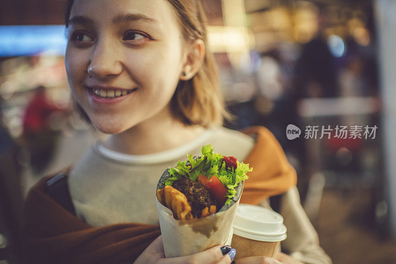 快乐的年轻女孩吃街头食物夏华马在晚上的城市夏天