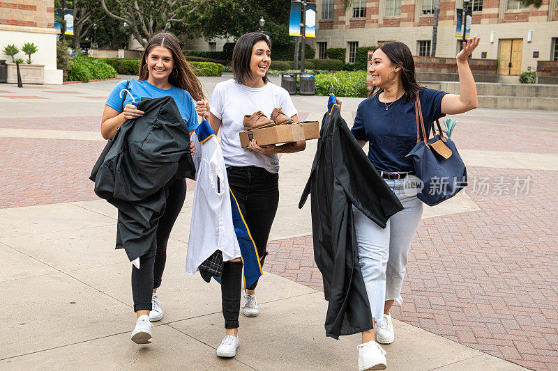 三名女大学毕业生拿着学士帽和学士服走路