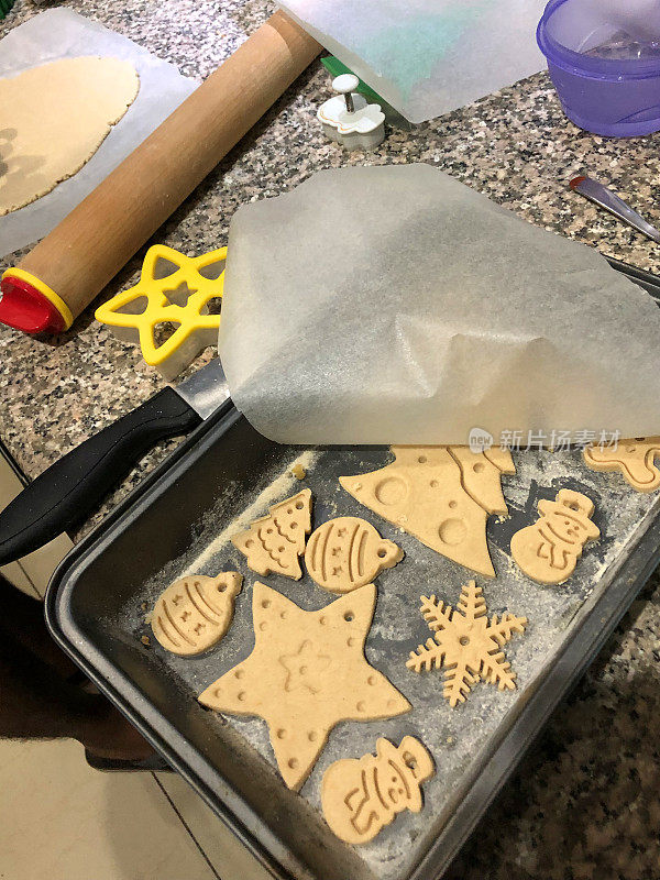 这是在厨房里用饼干切刀制作的新鲜烤制的圣诞饼干，从盐生面团到手工烤制，再到装饰圣诞树的手工彩绘，还有烤炉托盘上的圣诞树、姜饼人、星星、雪人