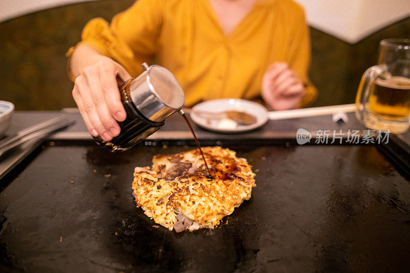 年轻女子把酱汁倒在煎锅上的御膳烧上