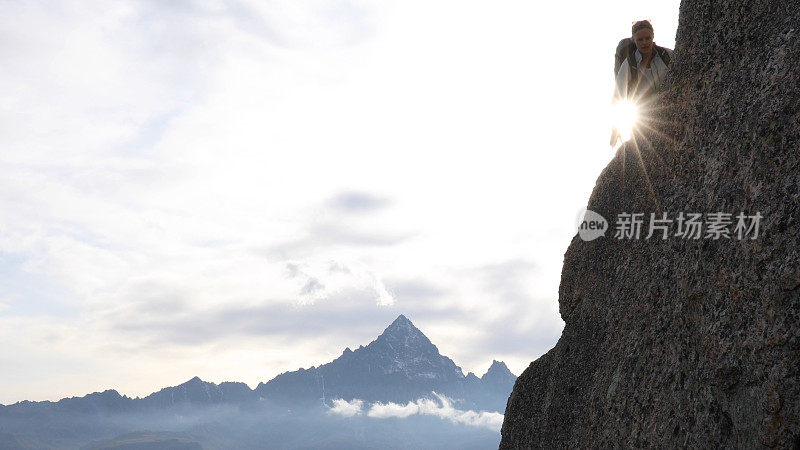 日出时，一位女登山运动员站在岩壁上眺望远方的景色