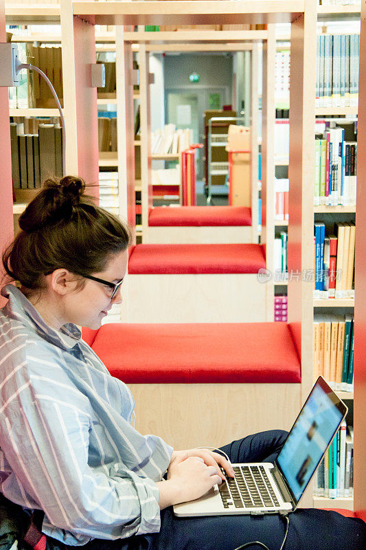 年轻女学生在图书馆使用笔记本电脑