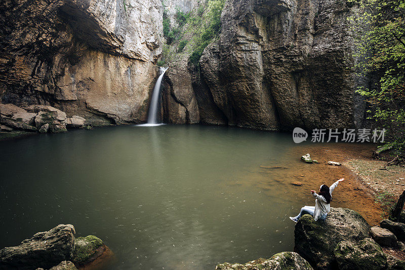 幸福的女人举起双臂，在美丽的瀑布旁享受生活